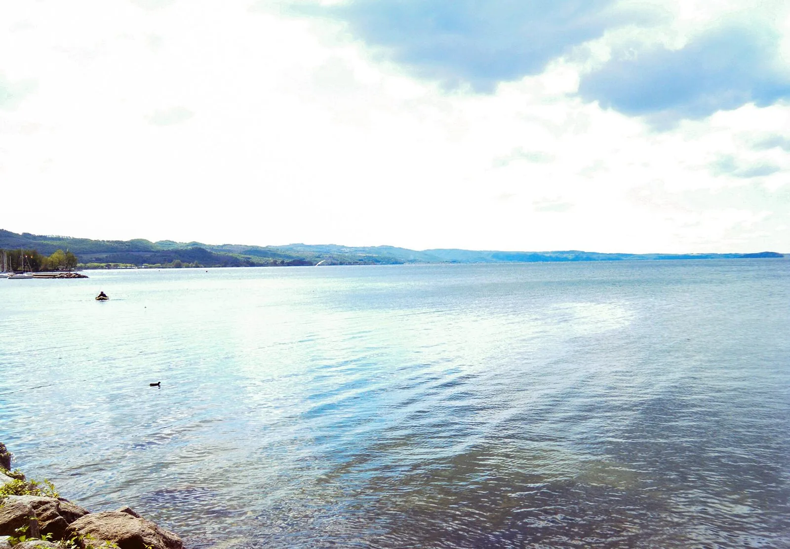 Il lago di Bolsena visto dal lungolago, acqua calma, colline sulla sponda opposta e cielo nuvoloso