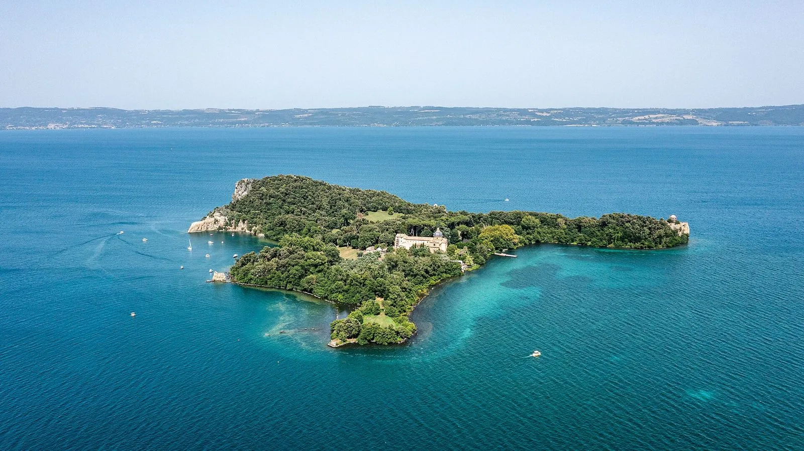 Veduta aerea dell'Isola Bisentina nel lago di Bolsena, coperta di boschi, con la chiesa a cupola e l'acqua turchese intorno