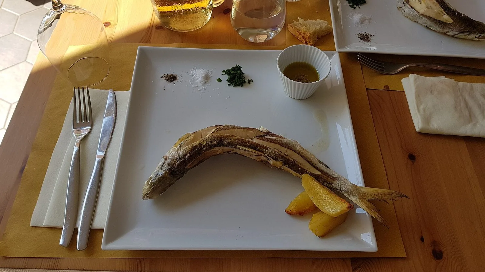 Un coregone del lago di Bolsena cotto intero e servito su un piatto bianco con patate, sale, pepe e prezzemolo